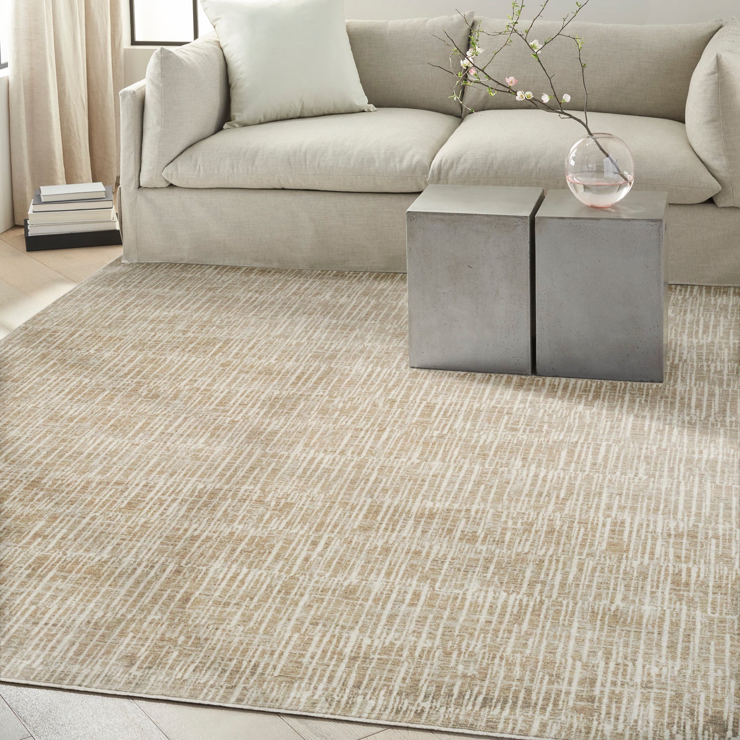 Beige fabric sofa with pale cushions, concrete block side tables, glass vase with blossoming branch, textured beige rug.