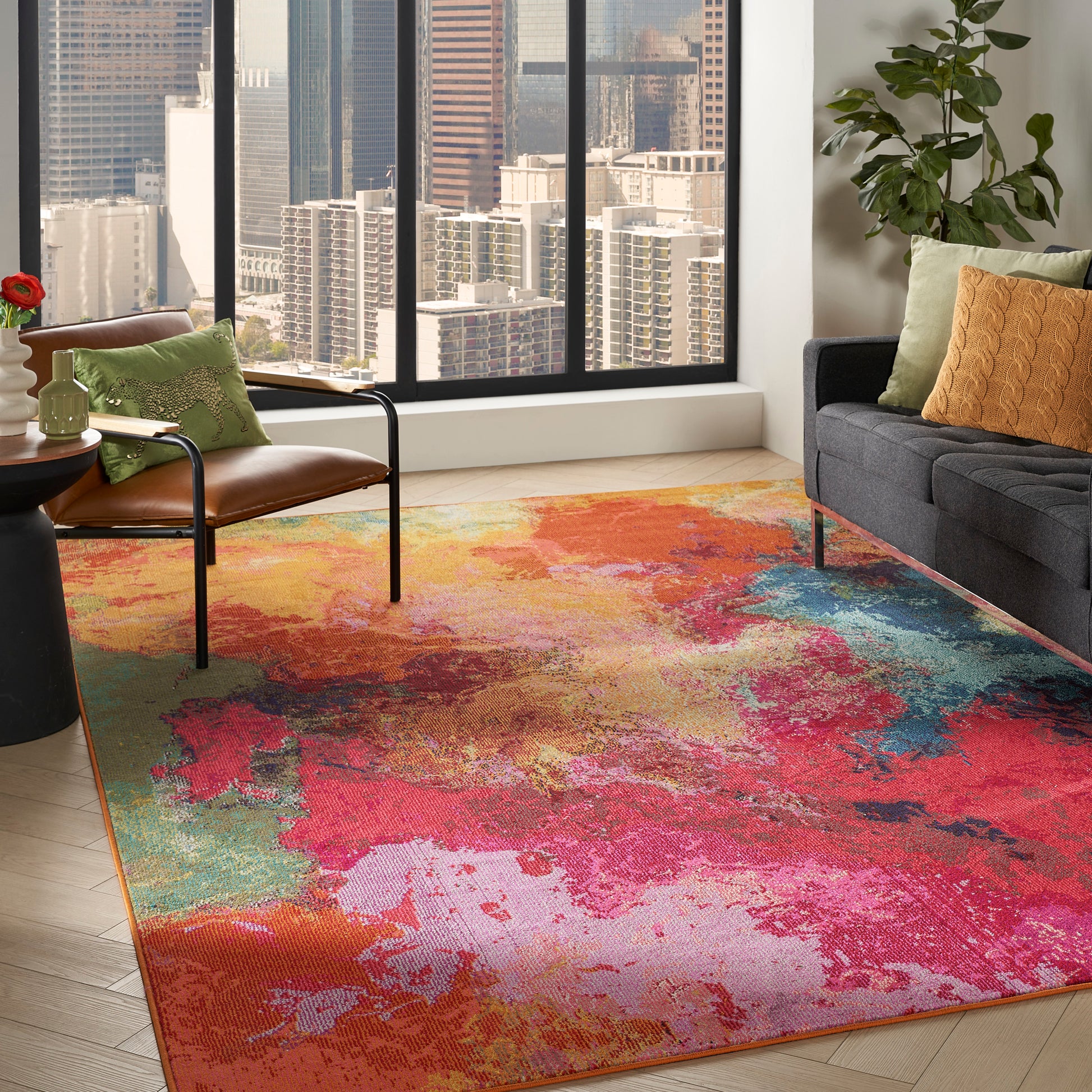 Rectangular abstract area rug with vivid pink, orange, yellow, blue and green hues; modern living room with gray sofa.