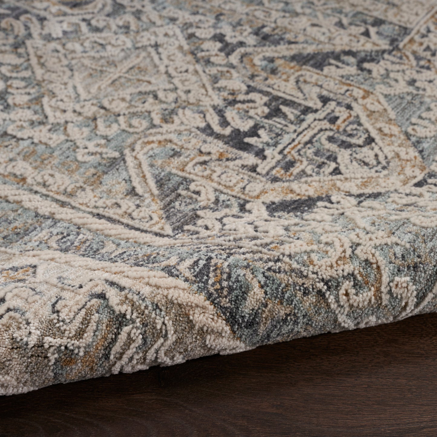 Close-up of a rectangular patterned rug in blue, beige, cream and gray with a distressed geometric motif on dark wood floor.