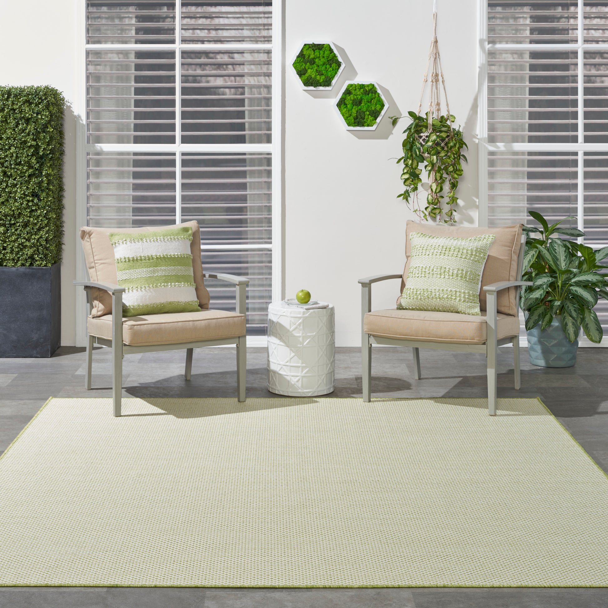 Outdoor patio with beige cushioned chairs, green striped pillows, rug, white side table, hexagon plant decor, and greenery.