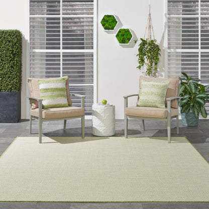 Outdoor patio with beige cushioned chairs, green striped pillows, rug, white side table, hexagon plant decor, and greenery.