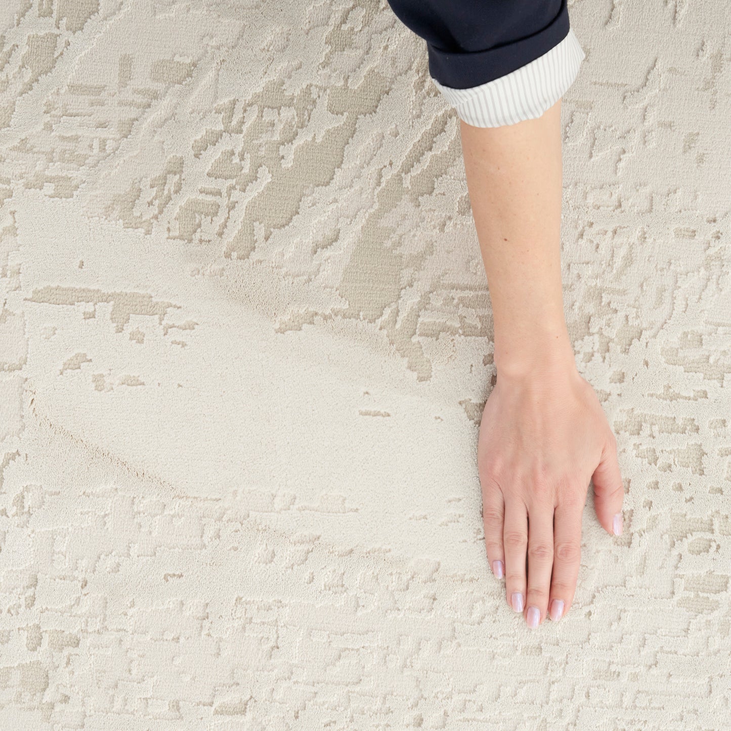 Hand resting on cream-beige textured rug; dark navy sleeve with white ribbed cuff visible.