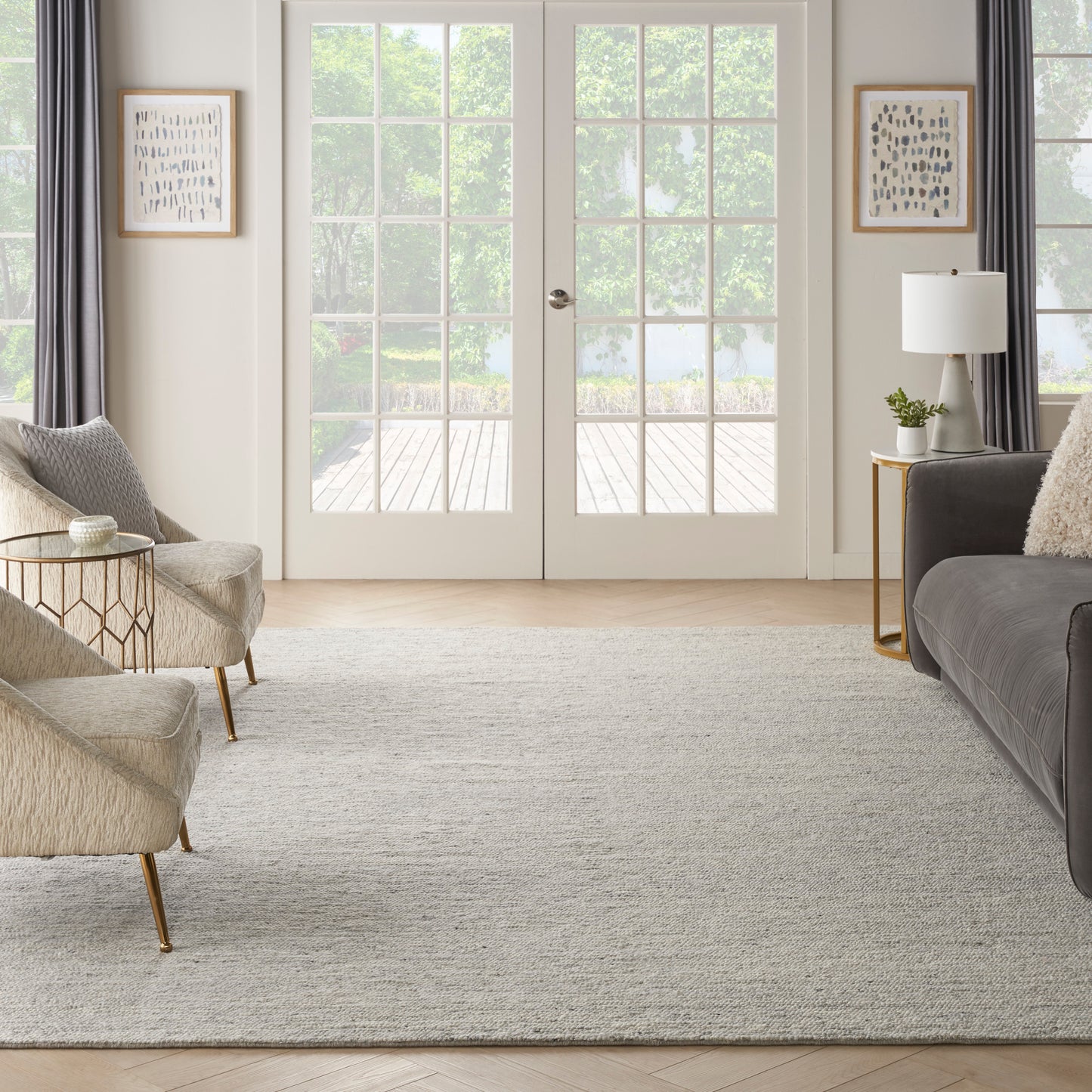 Bright living room with beige chairs, gray sofa, light rug, gold legs, glass side tables, white French doors.