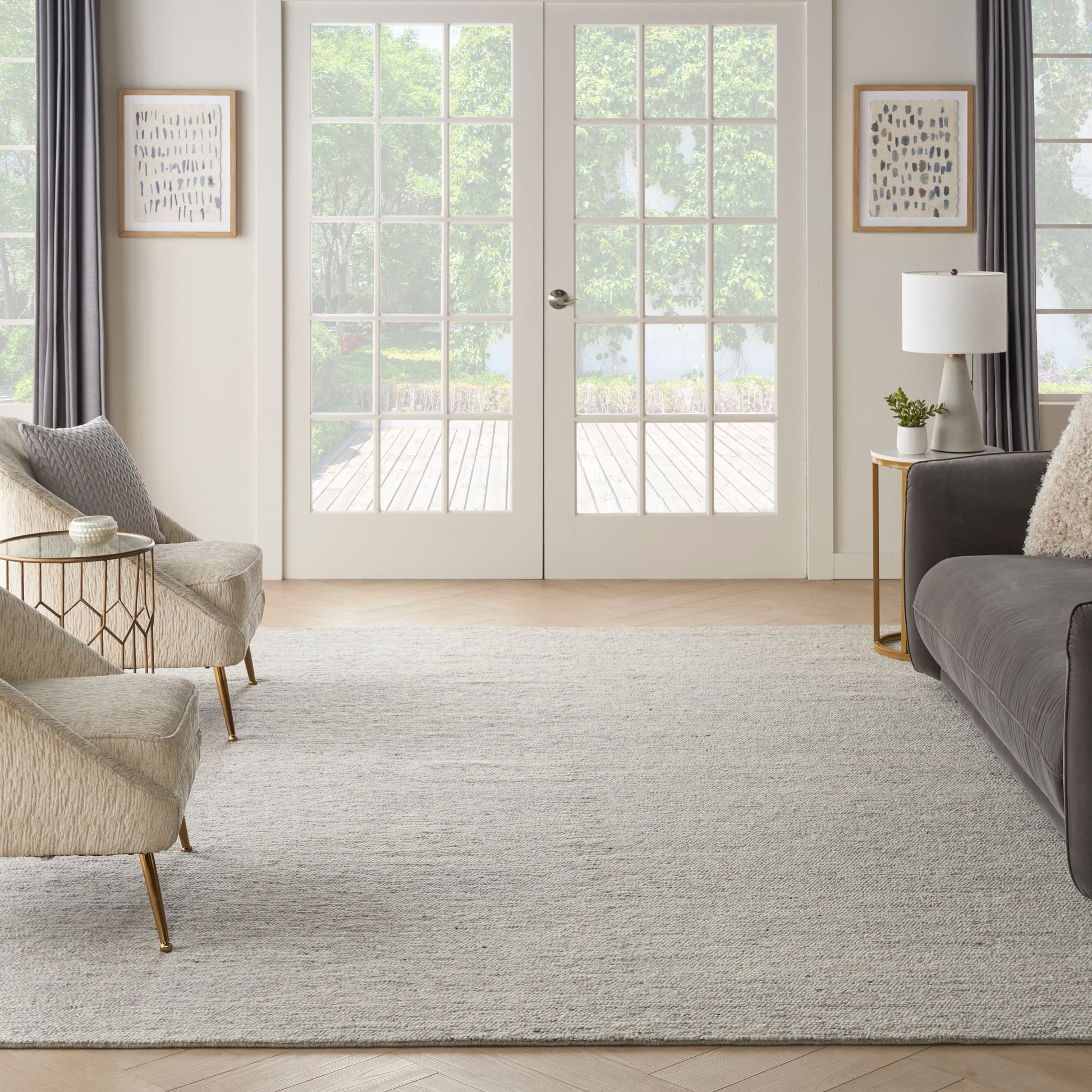 Bright living room with beige chairs, gray sofa, light rug, gold legs, glass side tables, white French doors.