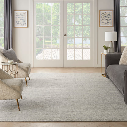 Bright living room with beige chairs, gray sofa, light rug, gold legs, glass side tables, white French doors.