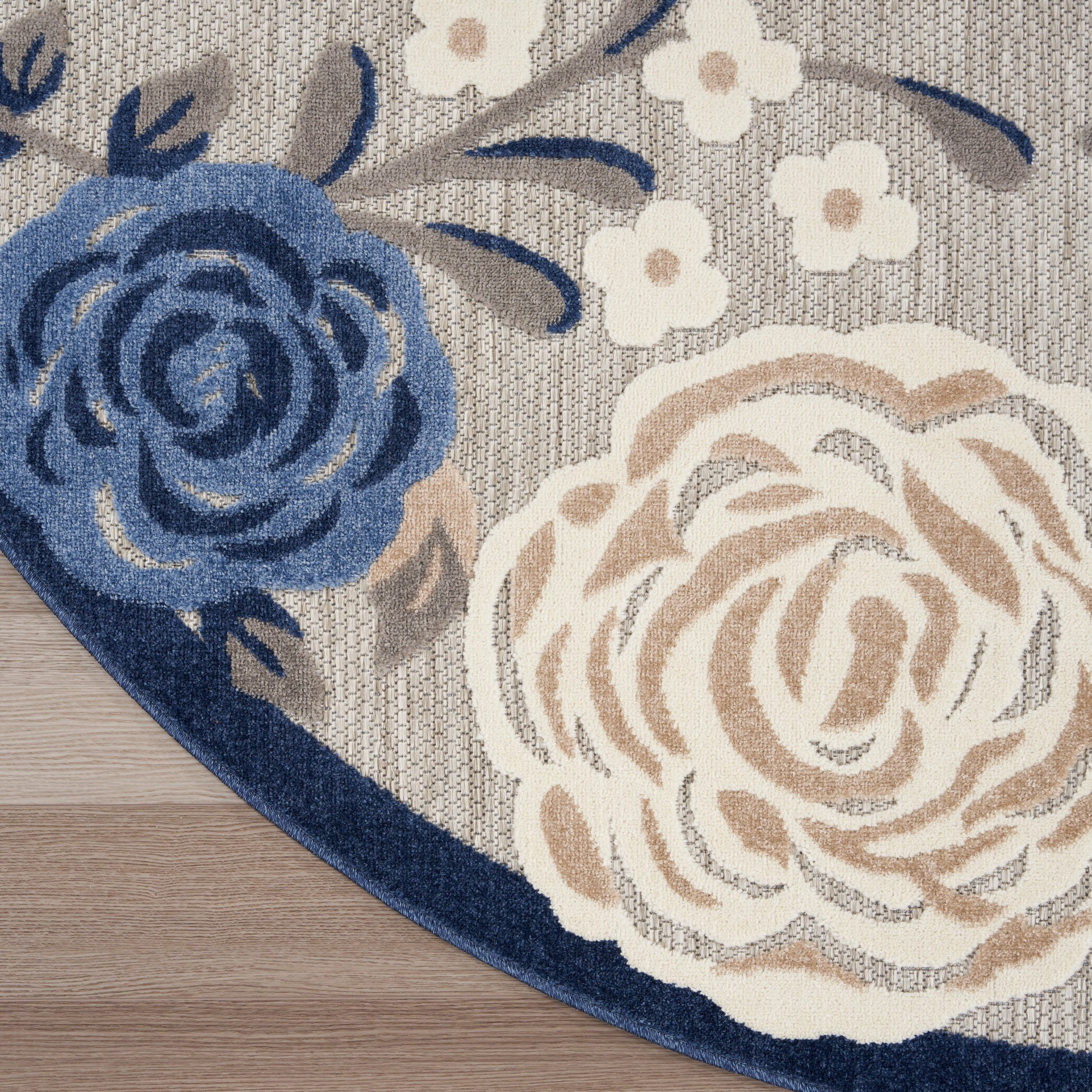 Round floral rug with blue and beige roses, small white blossoms, grey woven background and navy border on wooden floor.