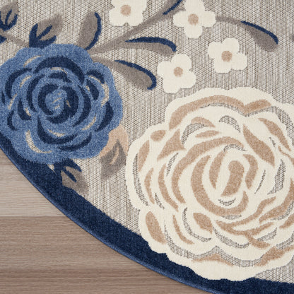 Round floral rug with blue and beige roses, small white blossoms, grey woven background and navy border on wooden floor.