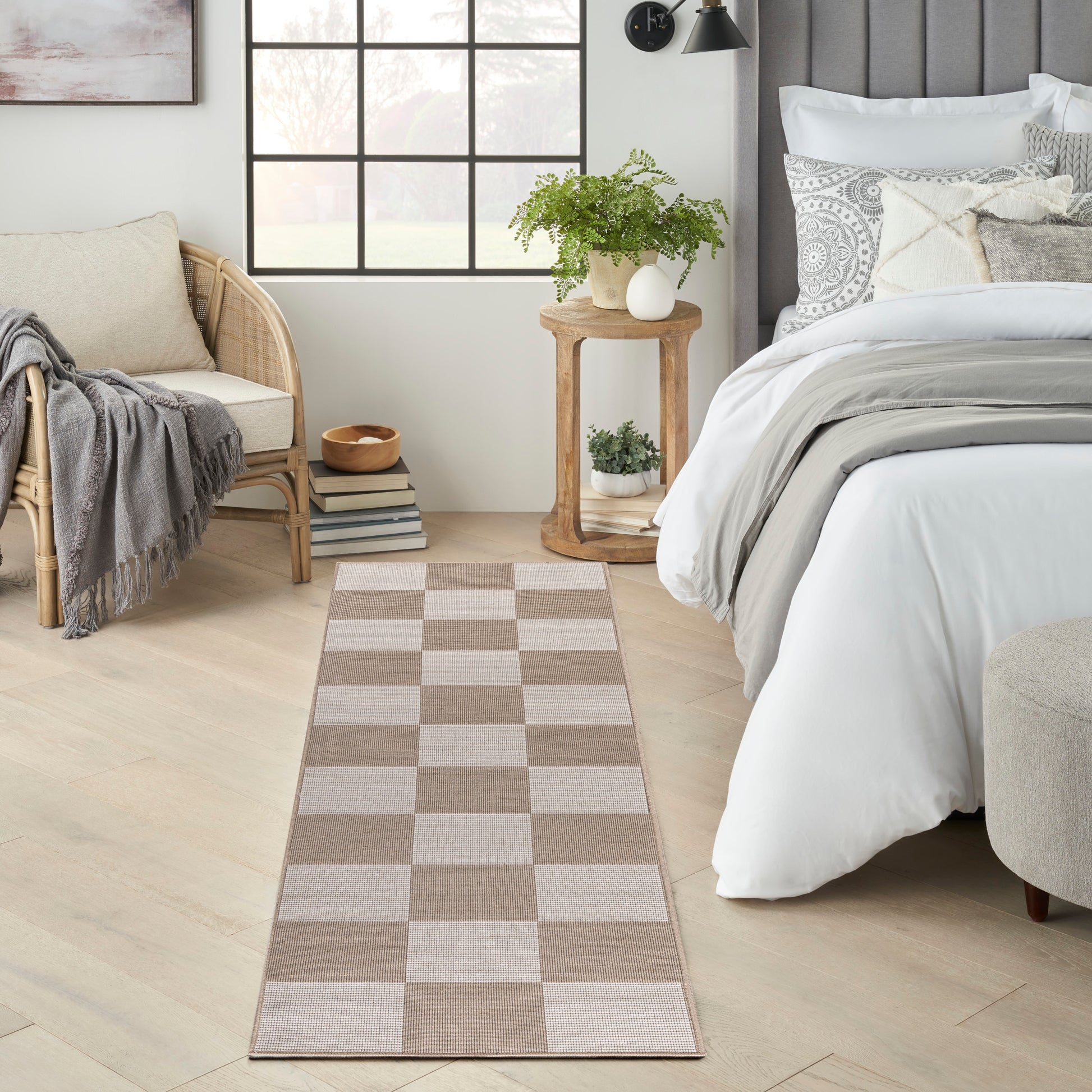 Beige and taupe woven checkerboard runner rug in a serene bedroom, placed beside the bed with a plant and wood table.