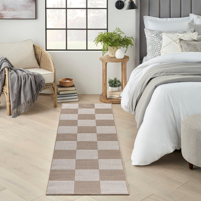 Beige and taupe woven checkerboard runner rug in a serene bedroom, placed beside the bed with a plant and wood table.