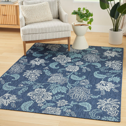 Blue floral patterned area rug with white and light blue blossoms, on hardwood floor beside a cream striped armchair.