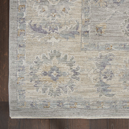 Rectangular rug with muted lavender, gray and beige floral medallions and border on dark hardwood floor.