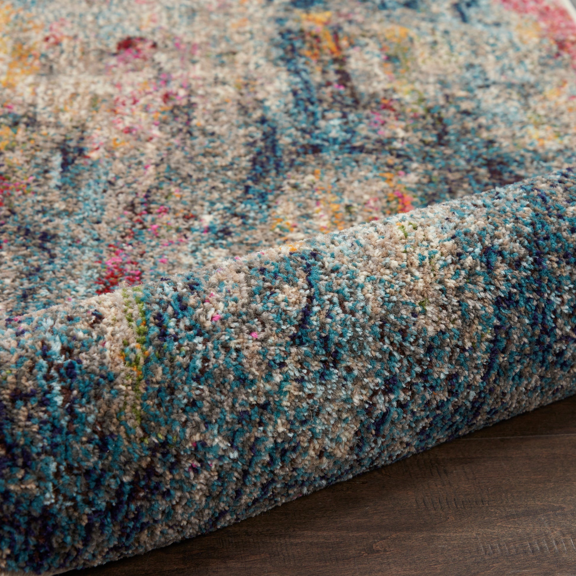 Colorful shag rug with dense multicolor pile in blues, teals, pinks, yellows on a cream base, rolled edge on dark wood floor