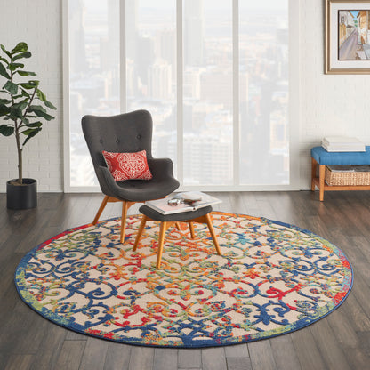 Round multicolor rug with blue, red and yellow motif under a grey mid-century chair and ottoman in a bright living room.