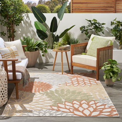 Outdoor patio with wooden chairs, cream cushions, green pillows, and a beige-orange patterned outdoor rug amid potted plants.