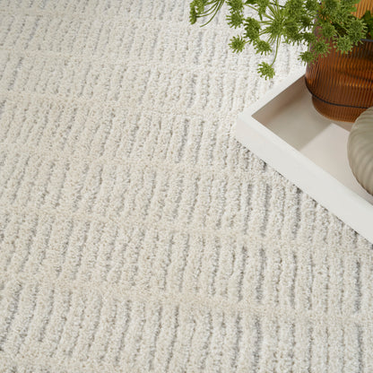 Cream textured rug with wavy linear pattern, white tray and brown ribbed vase with green plant for cozy home decor.