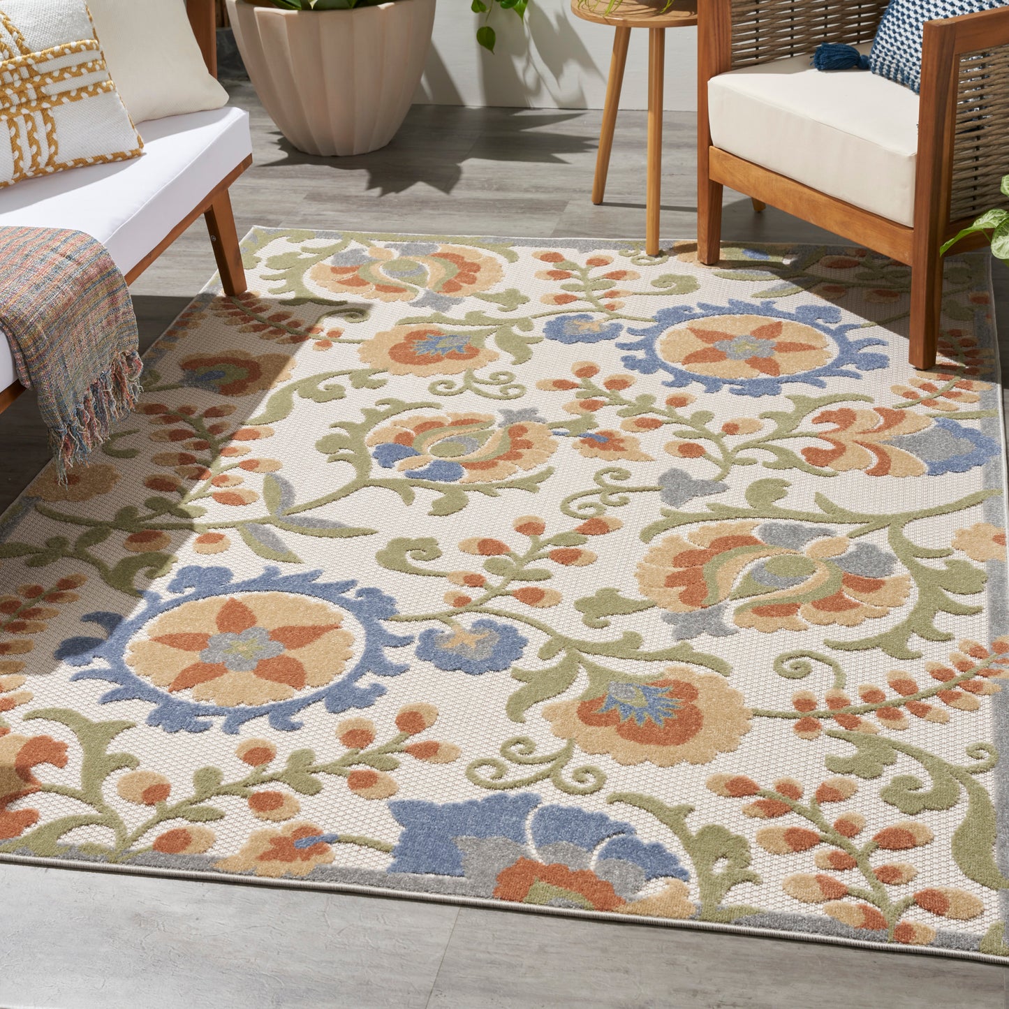 Outdoor floral area rug with cream background, olive green vines, orange and blue flowers; woven textured patio decor.