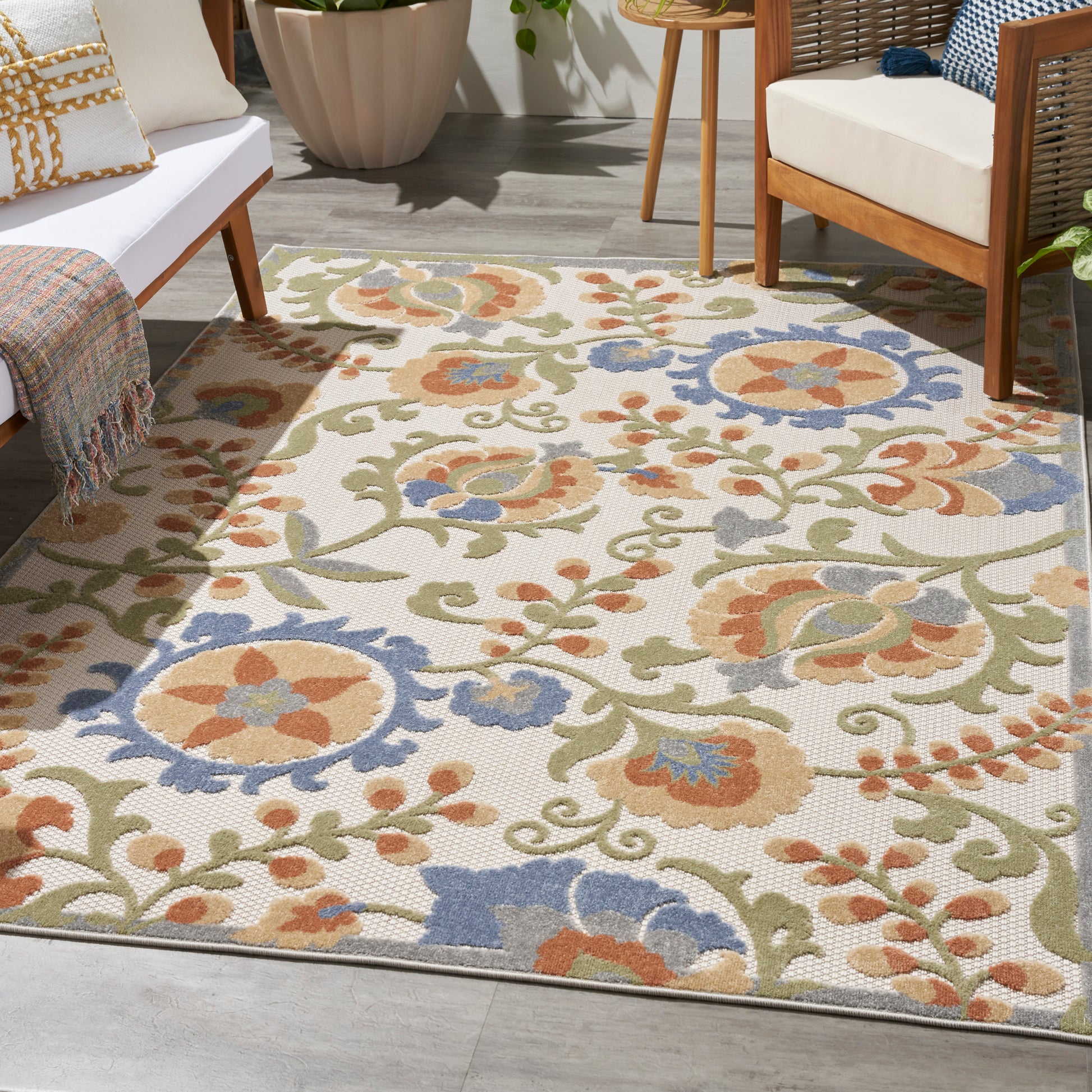 Outdoor floral area rug with cream background, olive green vines, orange and blue flowers; woven textured patio decor.