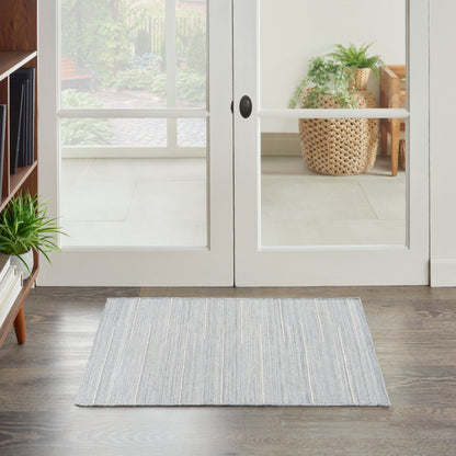 Light gray-blue striped rug on dark wood floor by glass doors; indoor plant and woven basket visible outside.
