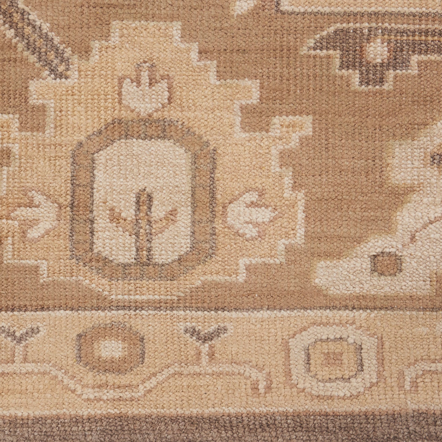 Beige and tan wool rug close-up with geometric medallion motif and decorative border in traditional oriental style.