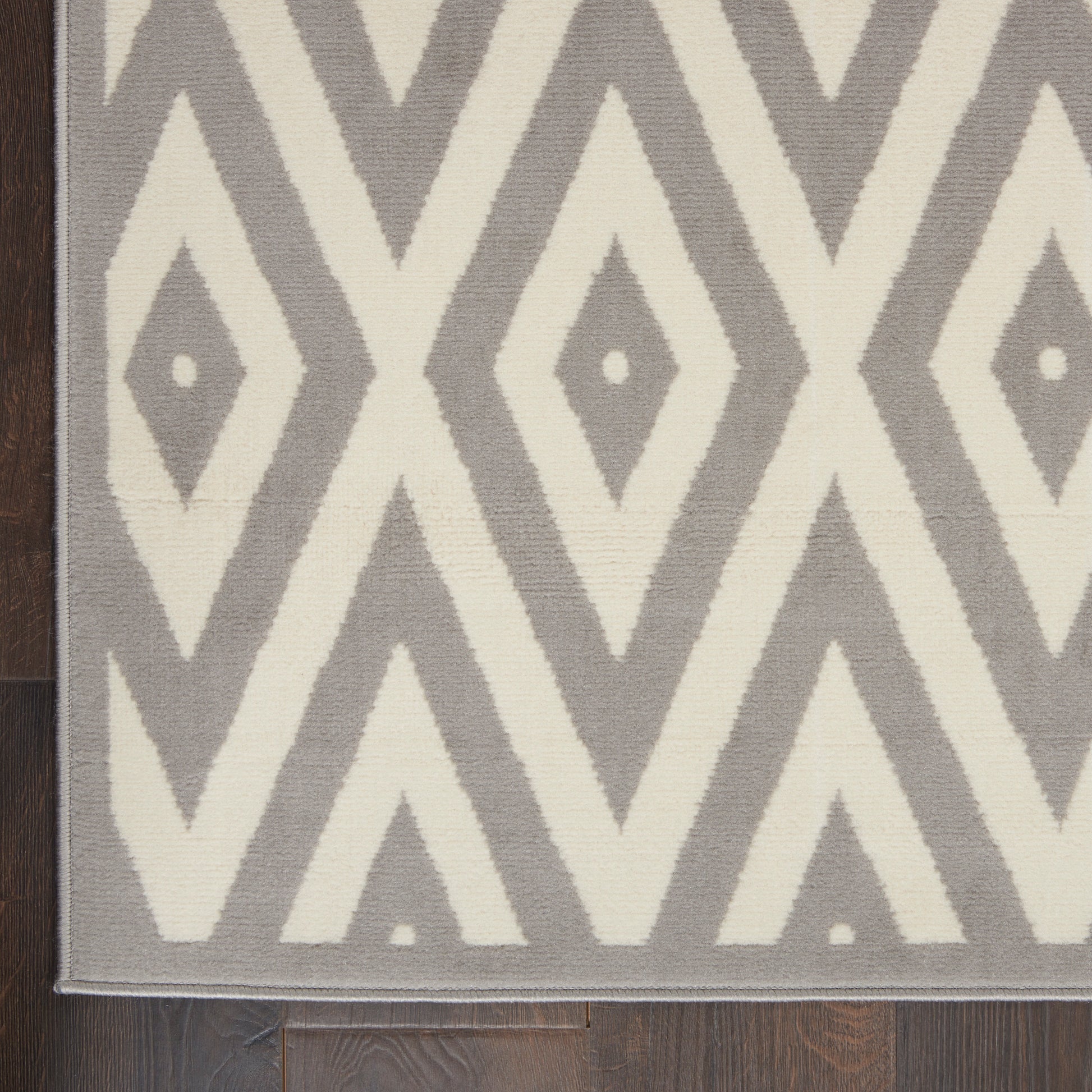 Gray and cream geometric rug with diamond motifs and chevron pattern on dark wood floor; light border.