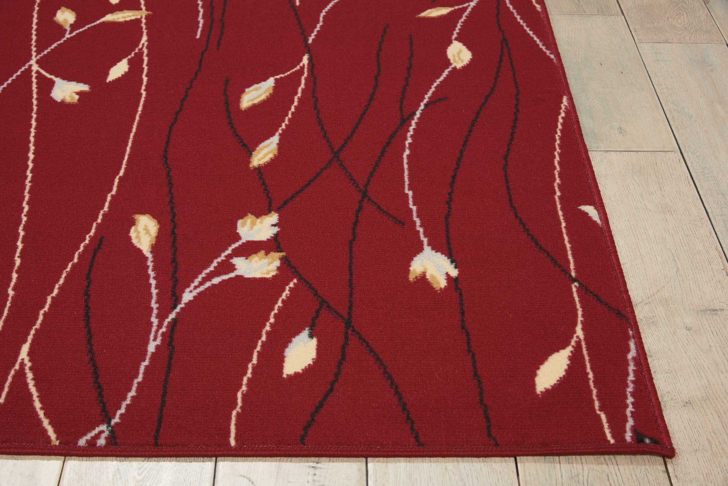 Red rectangular rug with white and black vine motifs and beige leaf accents on light wood floor.