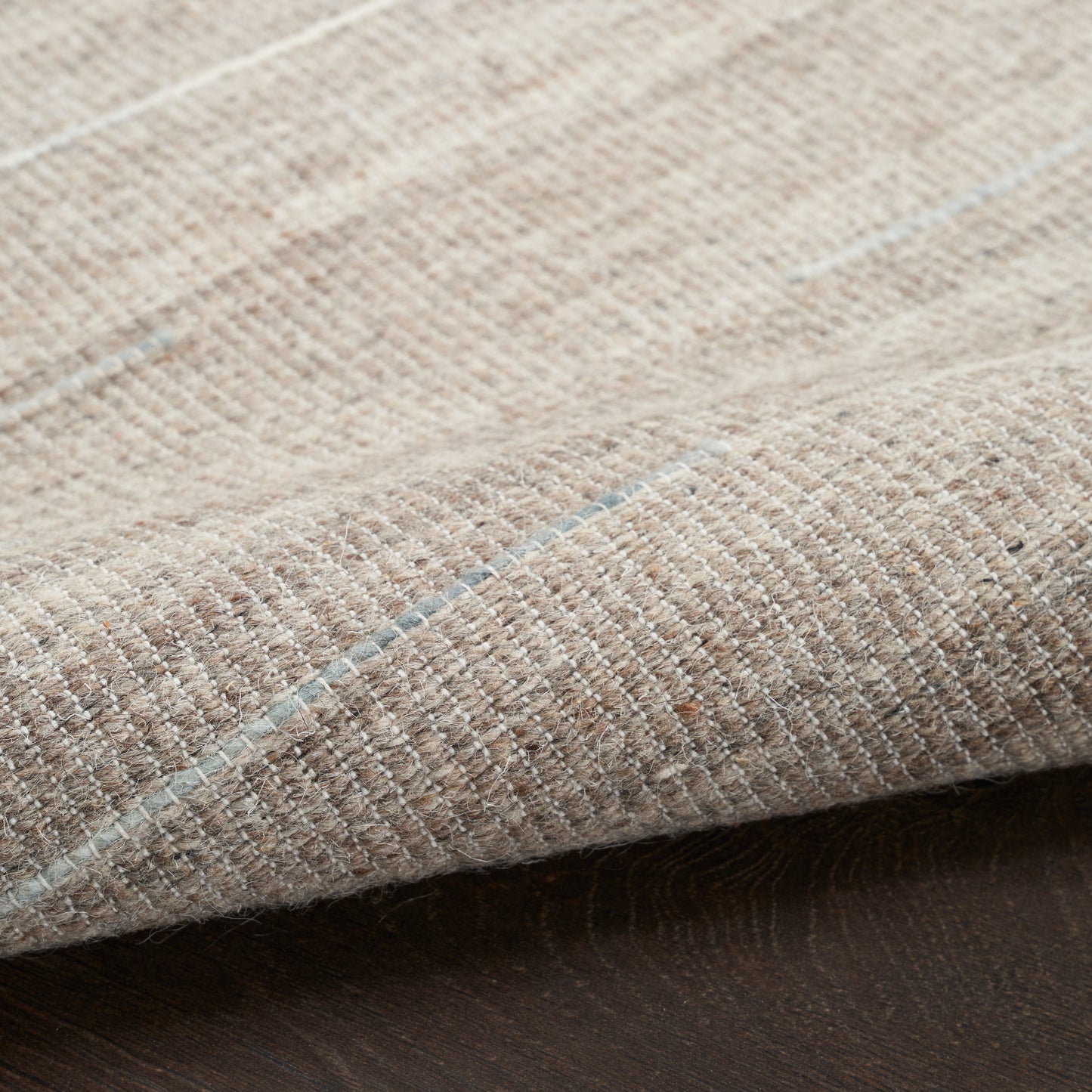 Beige woven rug with pale blue stripes; close-up shows textured fabric and folded edge.