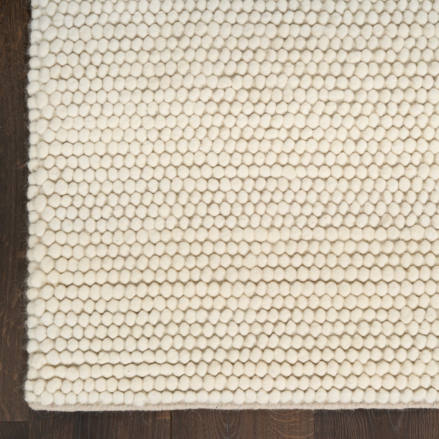 Cream boucle loop-pile rug on dark wood floor; textured cotton weave for cozy spaces.