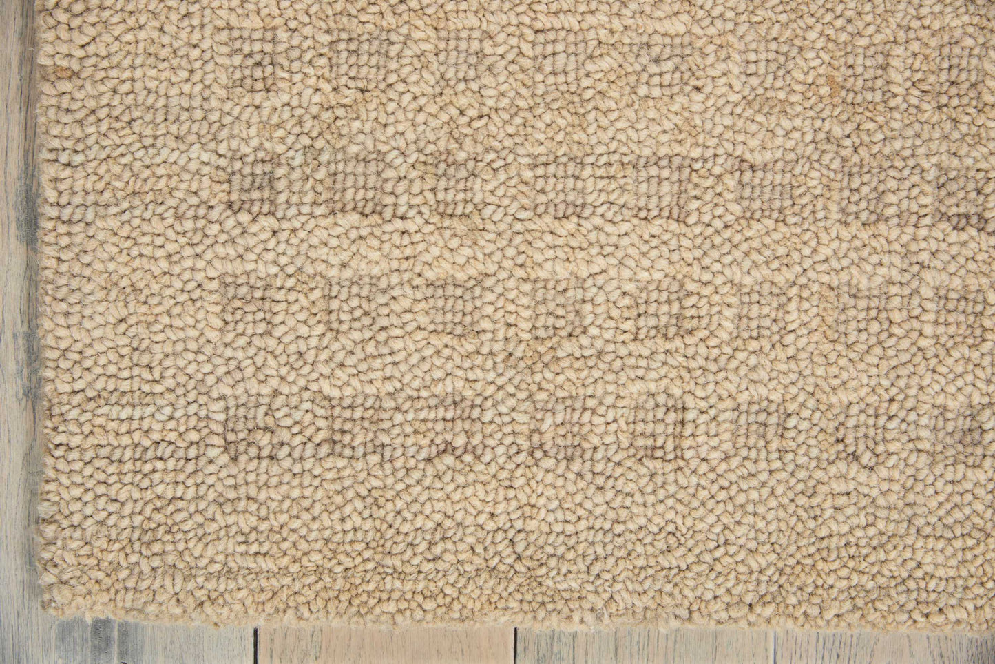 Beige shag rug close-up with dense loop pile on a light wooden floor edge.