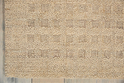 Beige shag rug close-up with dense loop pile on a light wooden floor edge.
