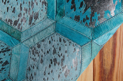 Close-up of teal hair-on-hide hex patchwork rug with black speckle pattern and visible stitching on a wood floor.