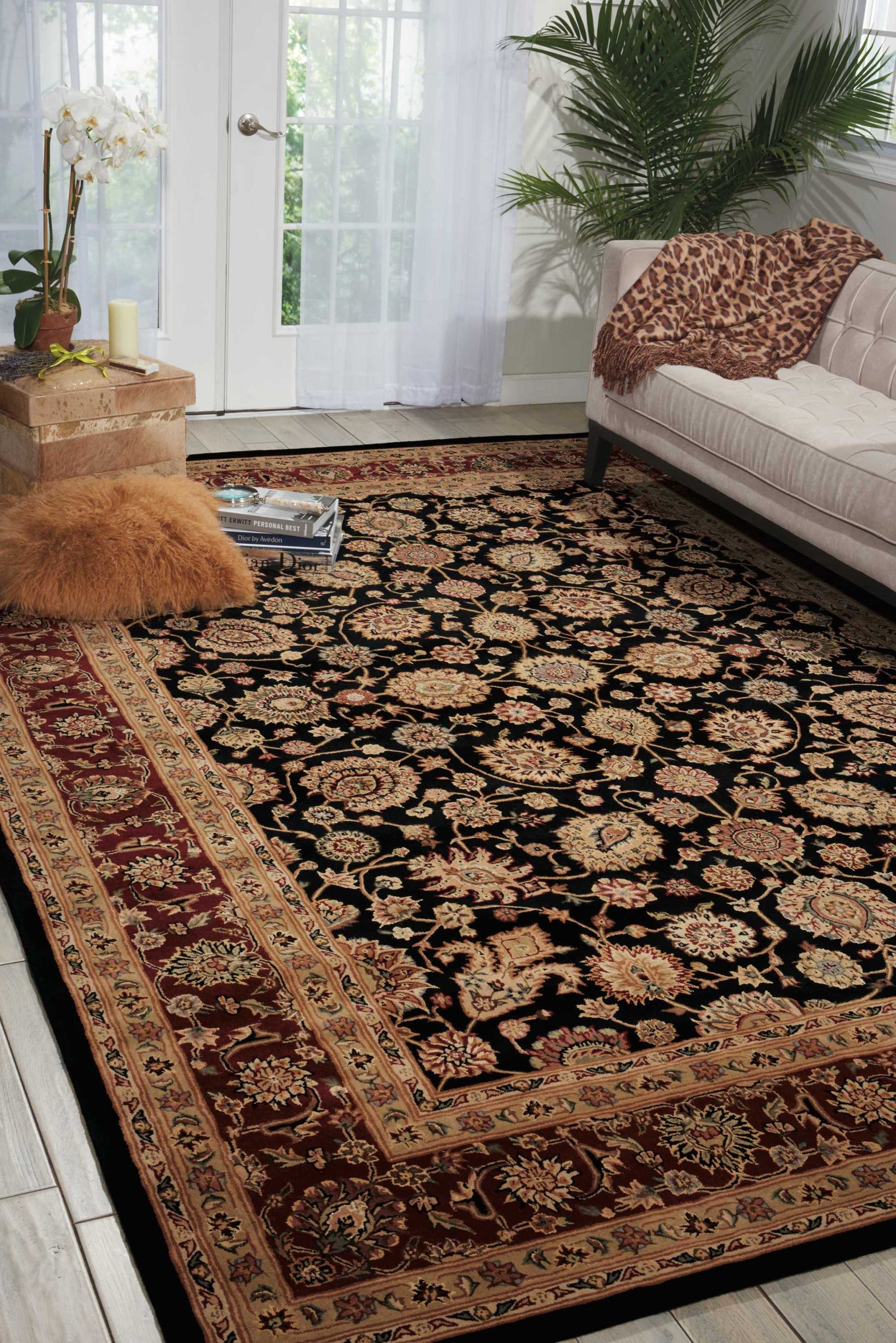 Living room with a black Persian-style rug with gold floral motifs and red/beige border; beige sofa, leopard-print pillow.