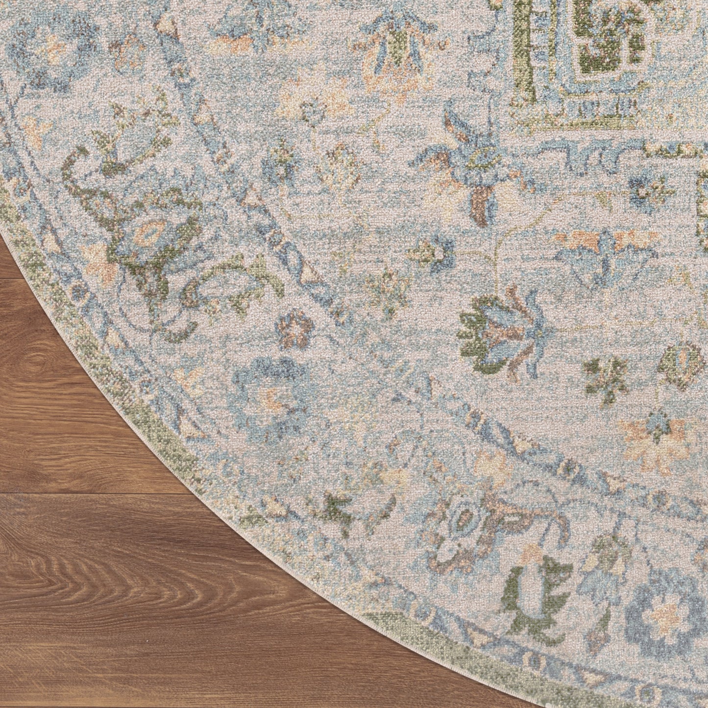 Round area rug with blue, ivory, and sage floral pattern on warm wood floor; vintage-style distressed motif.