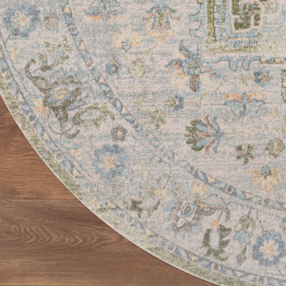 Round area rug with blue, ivory, and sage floral pattern on warm wood floor; vintage-style distressed motif.