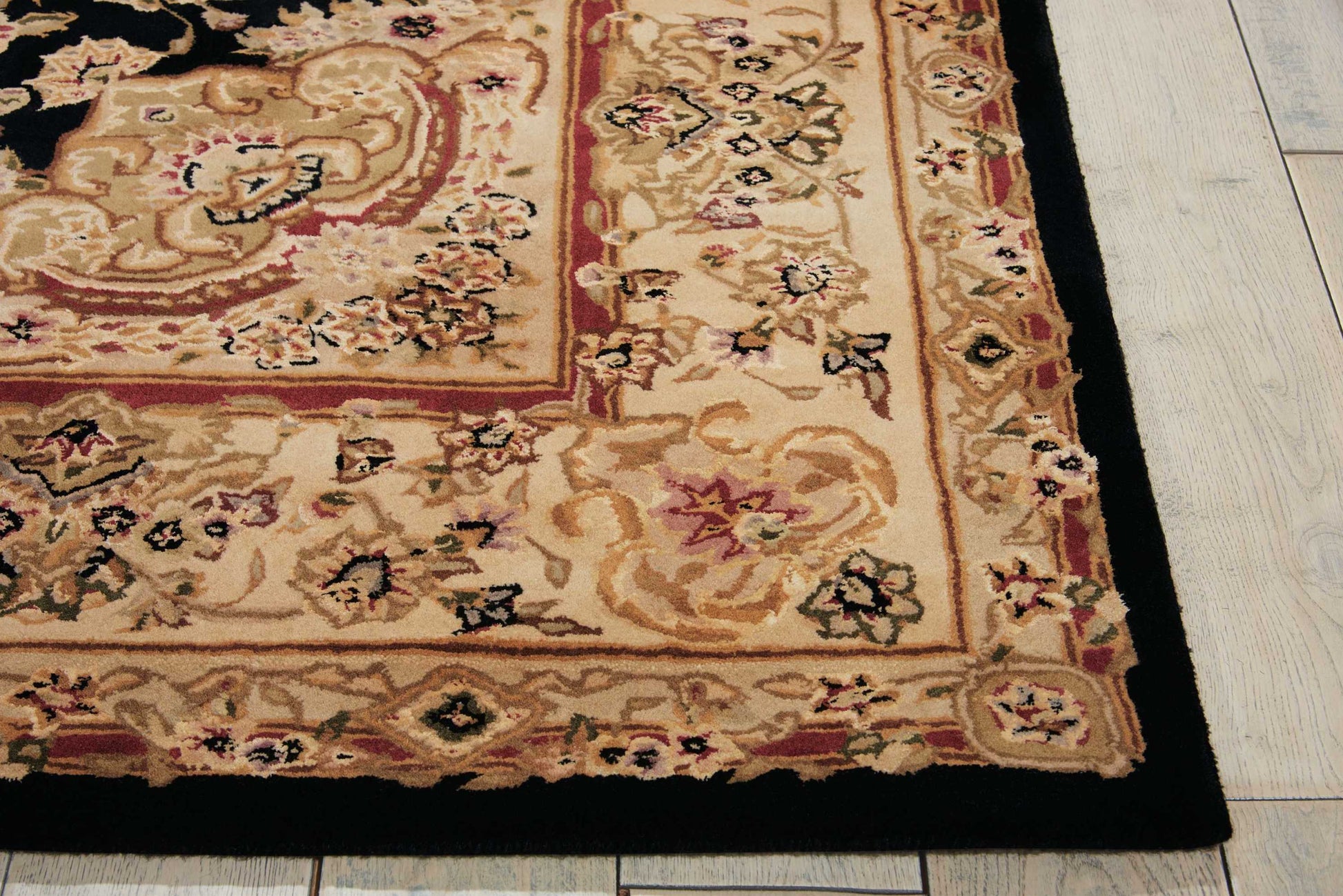 Partial view of an ornate beige Oriental rug with red border, black outer trim, floral motifs, on a wooden floor.