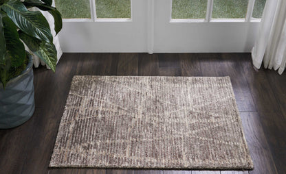 Neutral beige-brown rectangular rug with a subtle mottled pattern on a dark wood floor beside glass doors and a potted plant.