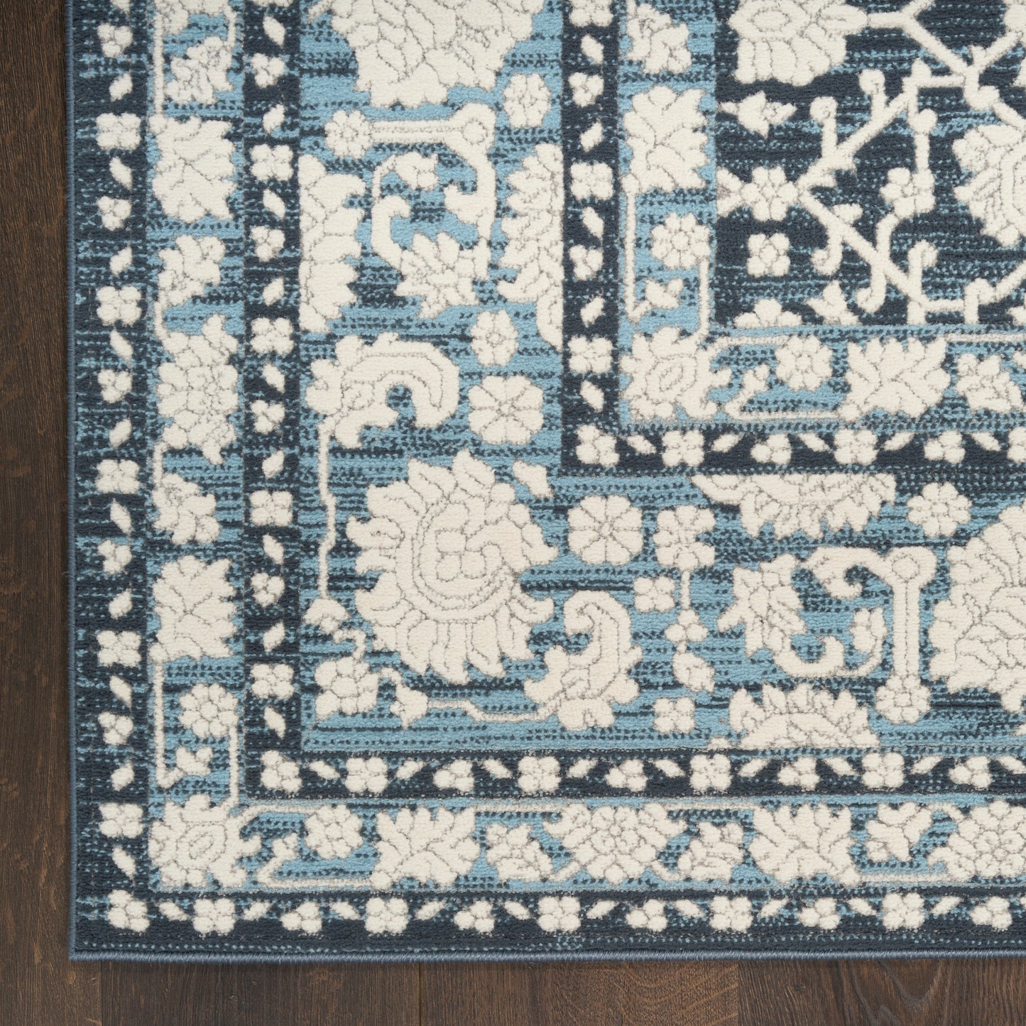 Blue and white oriental rug with floral borders on a dark navy field, laid on a wooden floor.