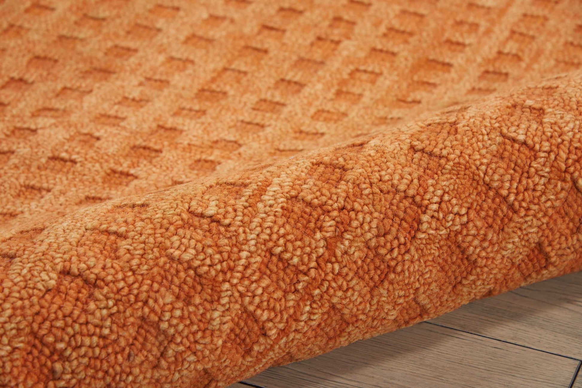 Orange shag rug with plush loop pile and subtle geometric diamond pattern, rolled on a wooden floor.