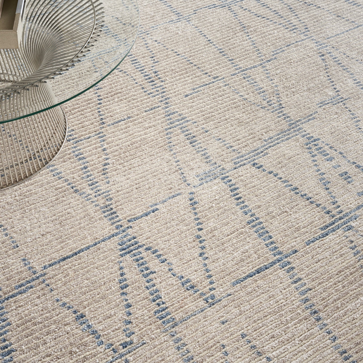 Beige textured area rug with light blue geometric grid pattern, paired with a glass round coffee table with a metal wire base.