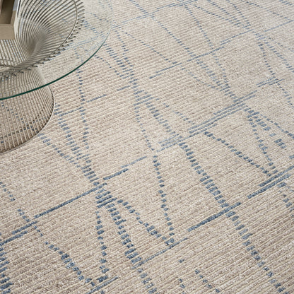 Beige textured area rug with light blue geometric grid pattern, paired with a glass round coffee table with a metal wire base.