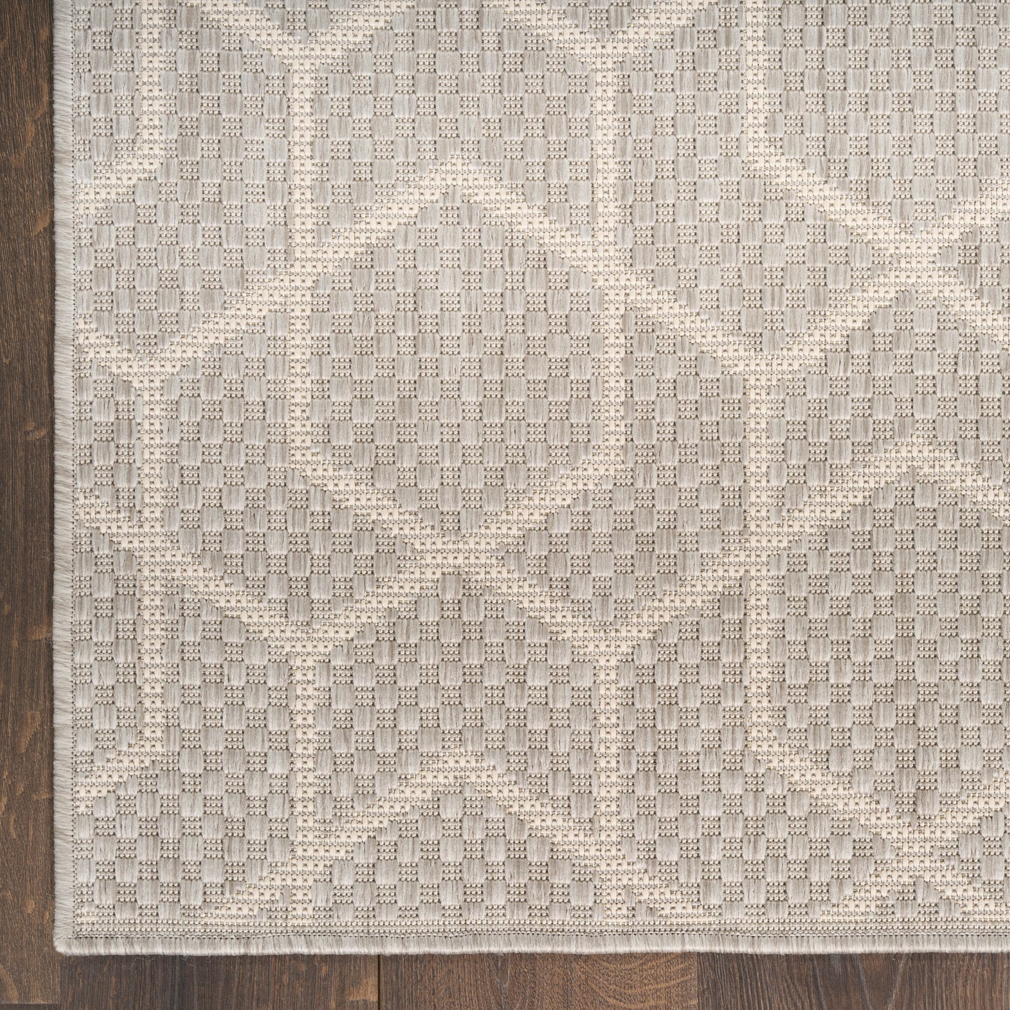 Beige and cream geometric rug with interlocking diamond trellis pattern on dark wood floor.