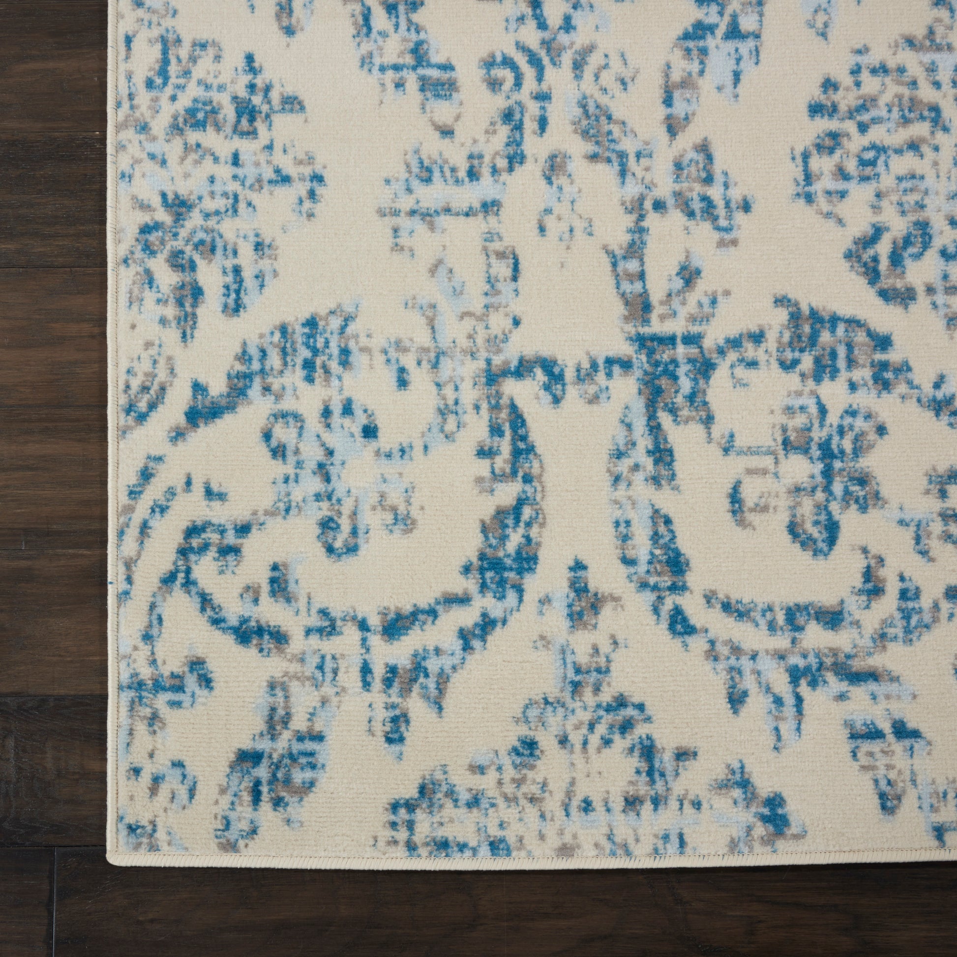 Cream rug with blue distressed damask pattern on dark wood floor; rectangular decorative area rug.