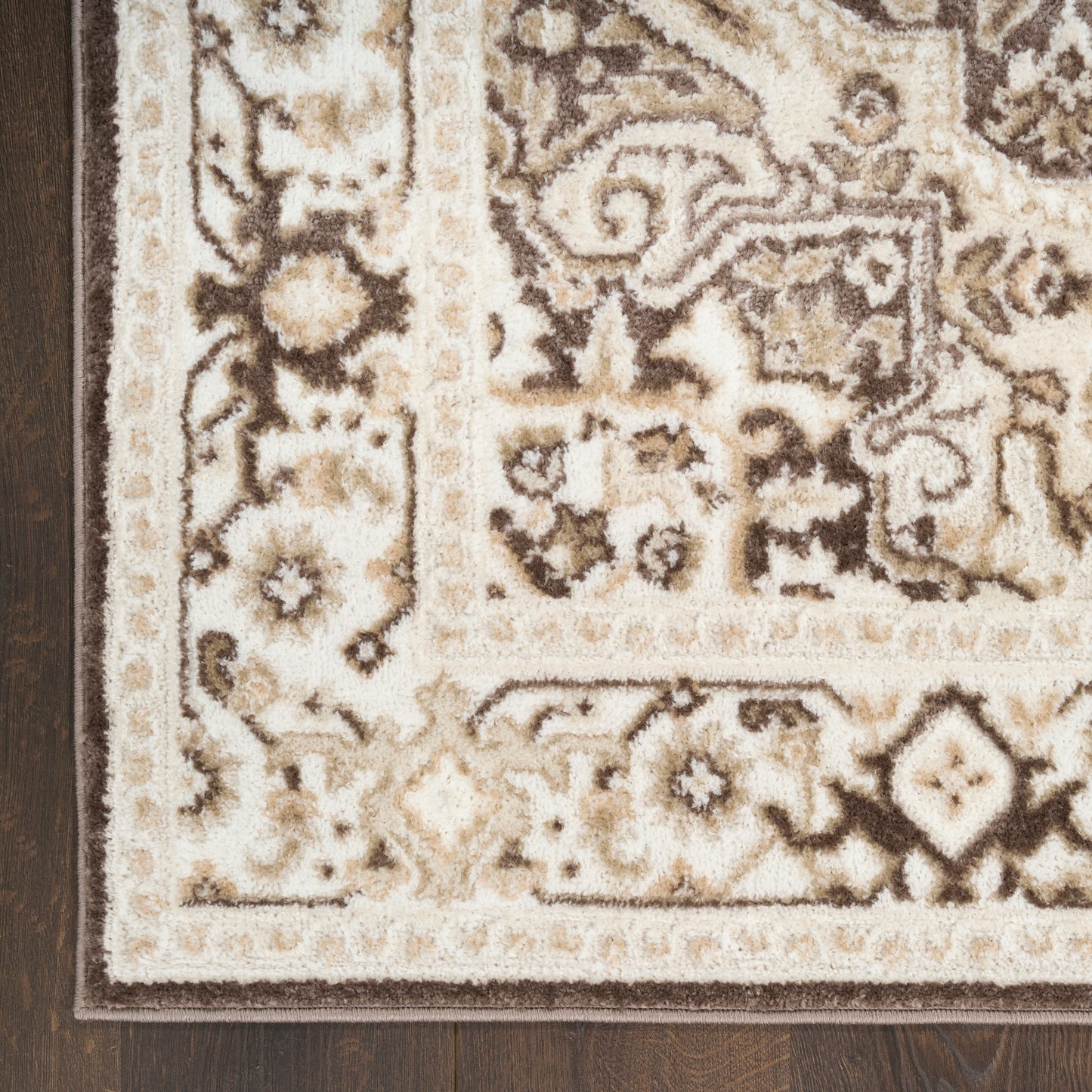 Rectangular beige-brown oriental rug with floral patterns and layered borders on dark wood floor.