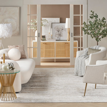 Neutral living room with a woven-front console, white seating, glass-topped side table, soft gray rug, plants and framed art.