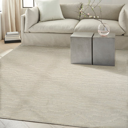 Beige sofa with two square concrete side tables, glass vase with branches, and cream rug in a neutral living room.
