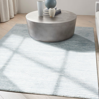 Round concrete-look coffee table on a pale blue striped rug with vases and books.