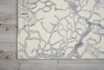Cream rug with pale gray abstract botanical lattice pattern on light wood floor.