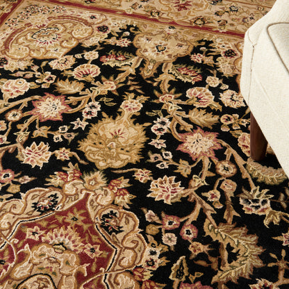 Ornate floral area rug with black field, gold & cream vines, pink accents; partial cream sofa leg visible.