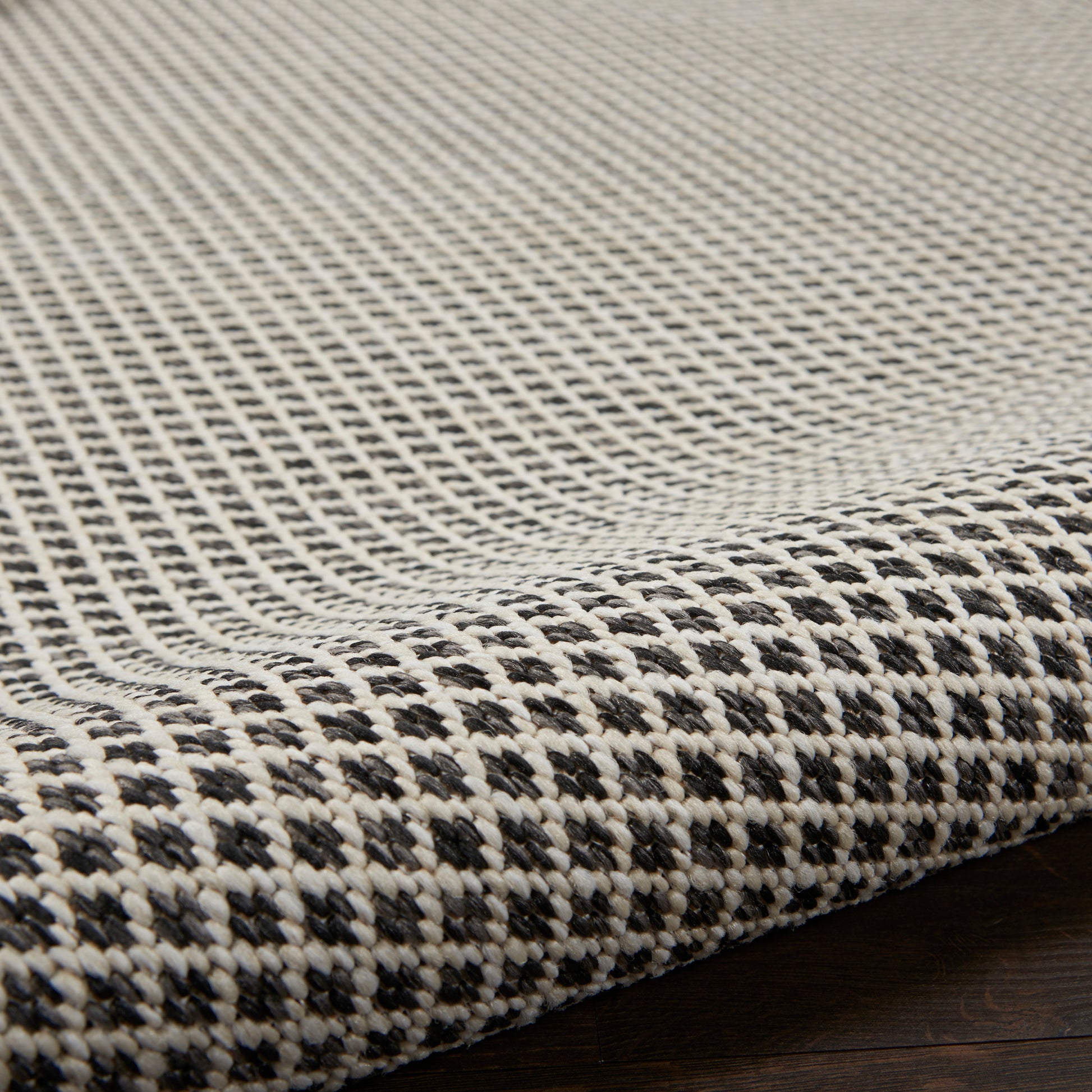 Close-up of a black & ivory checkered woven rug edge on dark wood floor.