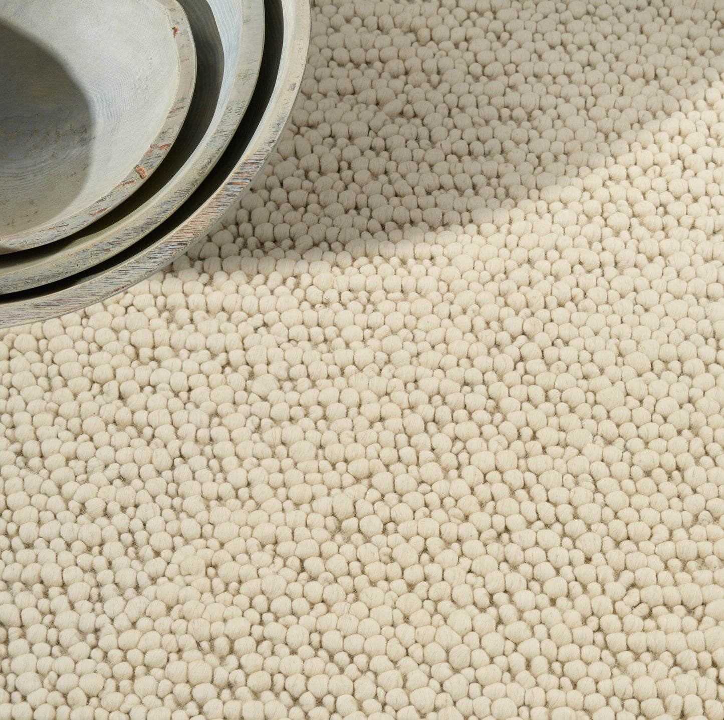 Beige boucle rug with rolled edge, cream textured loop-pile, suitable for living rooms.