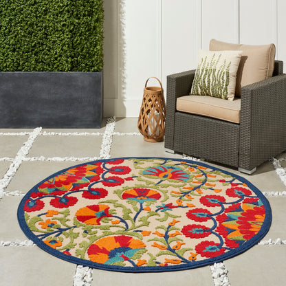 Round outdoor rug with a vibrant multicolor floral pattern and blue border on a stone patio beside a wicker armchair.
